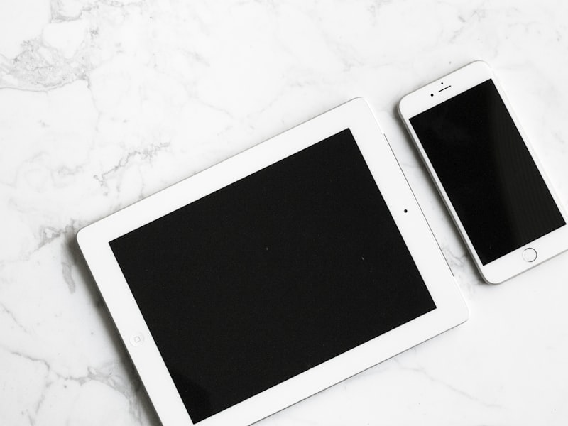 A tablet and a smartphone lying side by side on a white surface.